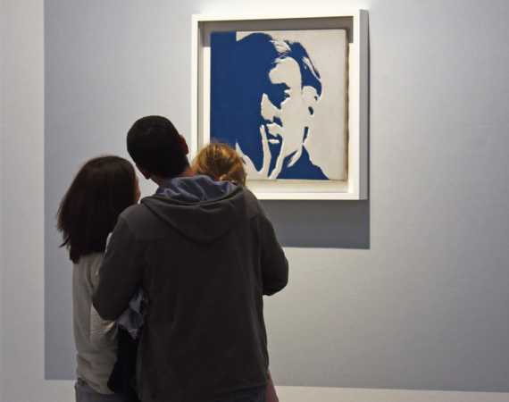 Un couple d'adulte tenant un enfant regarde un autoportrait d'Andy Warhol