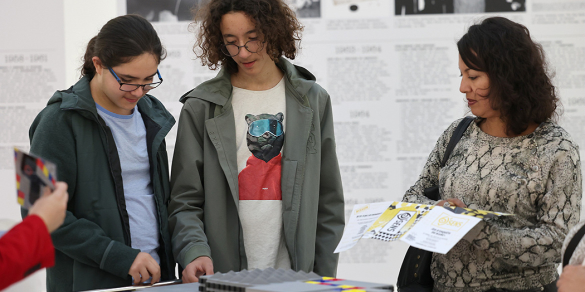 Trois visiteurs participant à un jeu d'enquête dans une salle d'expositions du musée