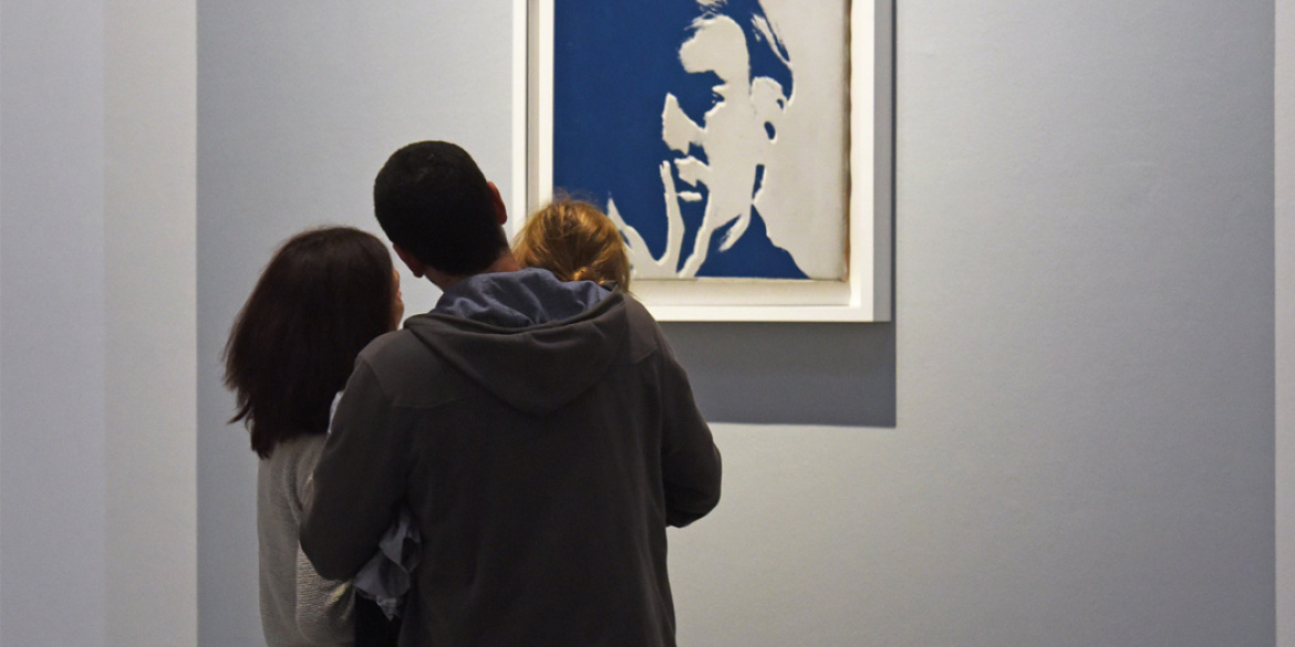 Un couple d'adulte tenant un enfant regarde un autoportrait d'Andy Warhol